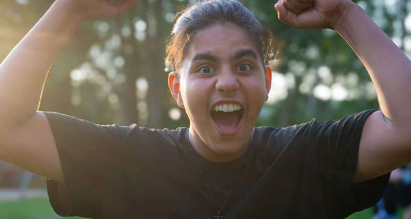 Nahaufnahme eines fröhlichen Jugendlichen mit erhobenen Armen im Ferienlager für Jugendliche.